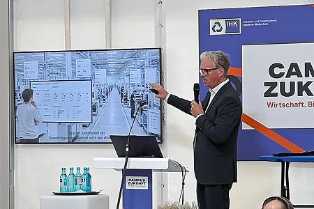 Ein Mann redet mit einem Mikrofon vor einem Bildschirm
